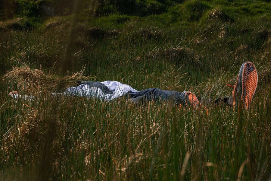 A figure lies largely obscured in a wide open field