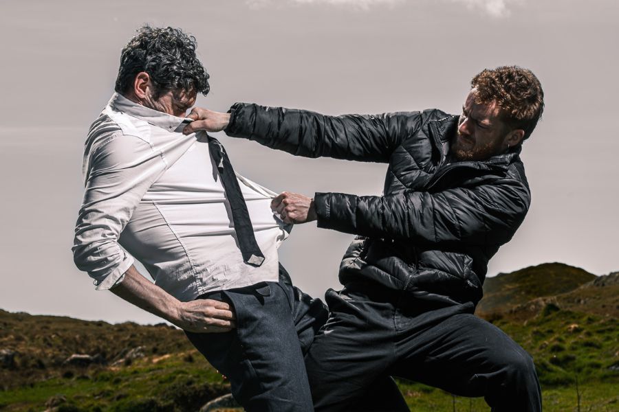 Two people pull at each other leaning back and counterbalancing, outdoors in a field