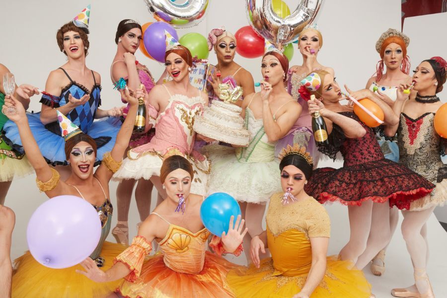 Group party photo of male ballerinas in bright colour tutus, holding balloons, party hats and a cake with a 50 sign on it