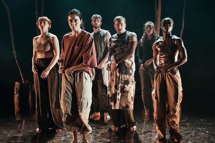 Six artists crouch down in a huddle against dark backdrop with warm lighting