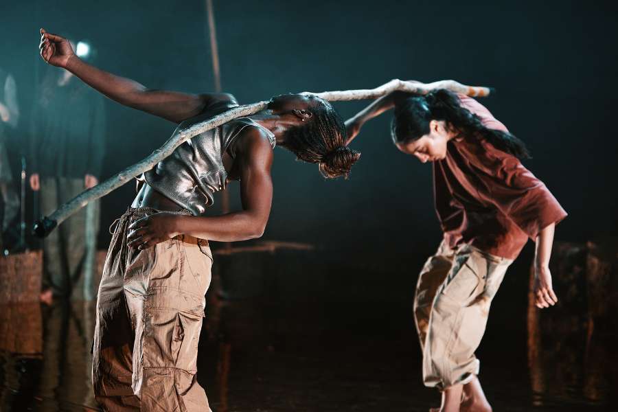 A dark stage with warm lighting illuminating the four dancers as they move