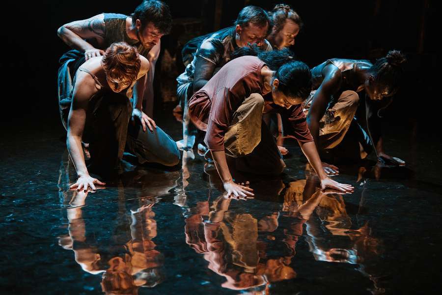 Group of people stand in a group in natural coloured clothing staring with intense expressions