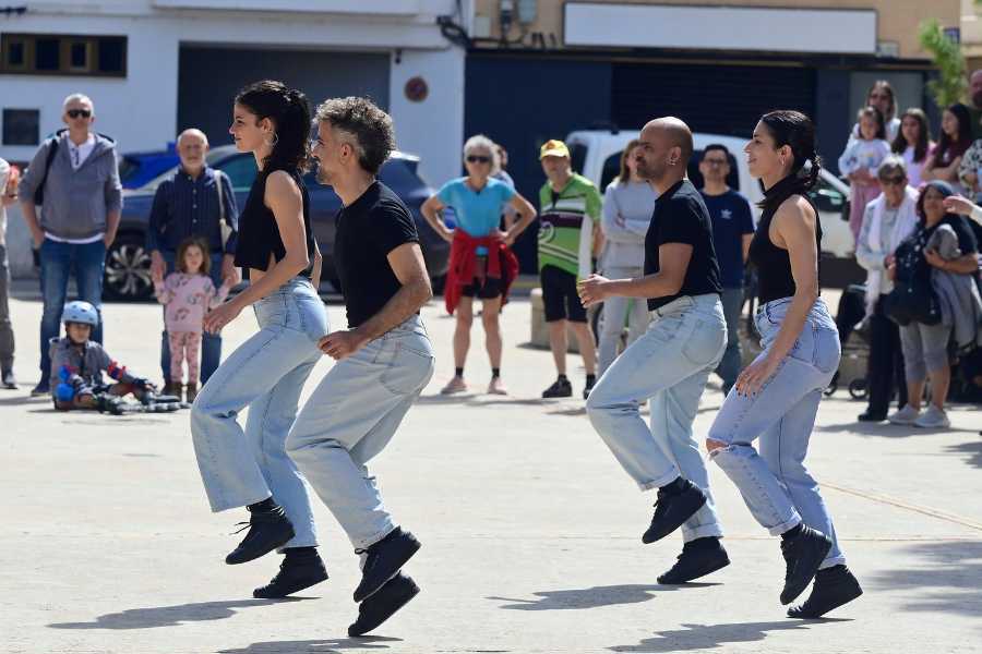 Four people in jeans and black tops perform in unison outdoors