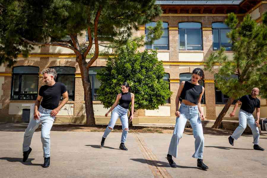 Four people in jeans and black tops perform in unison outdoors