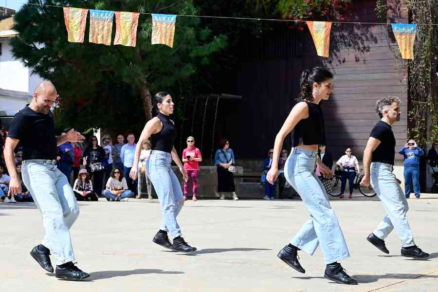 Four people in jeans and black tops perform in unison outdoors