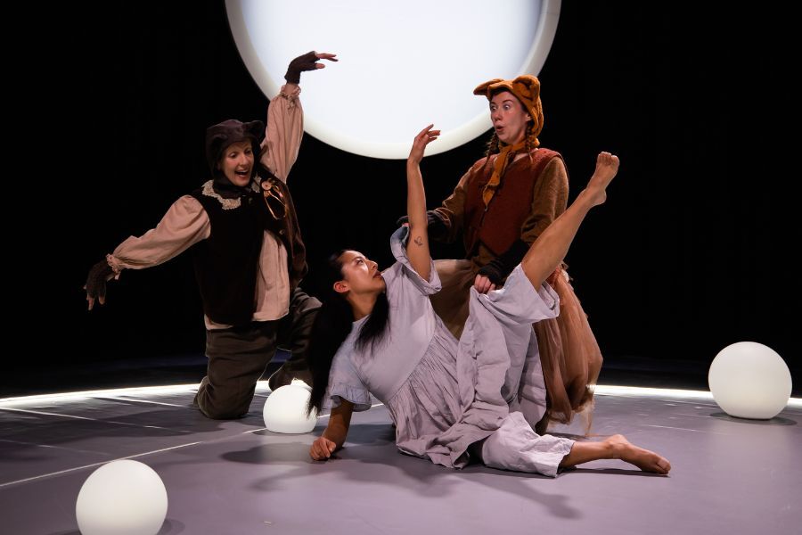 Three performers in a huddle on stage with a full moon behind them