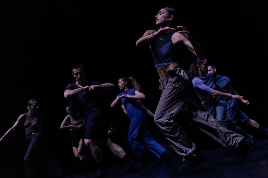Group of dancers move and leap with great energy against a dark background.