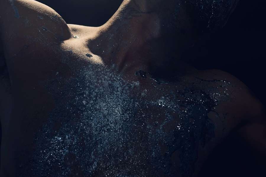 A splash of shiny silver paint against a dark background with a glimpse of a naked torso.