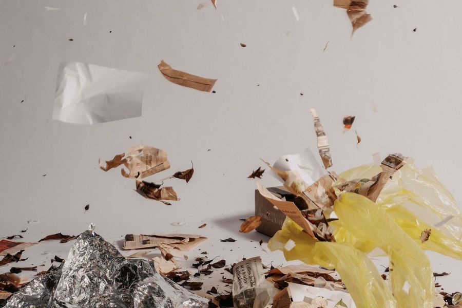 Plastic and paper debris blows in a strong wind in a stark white space