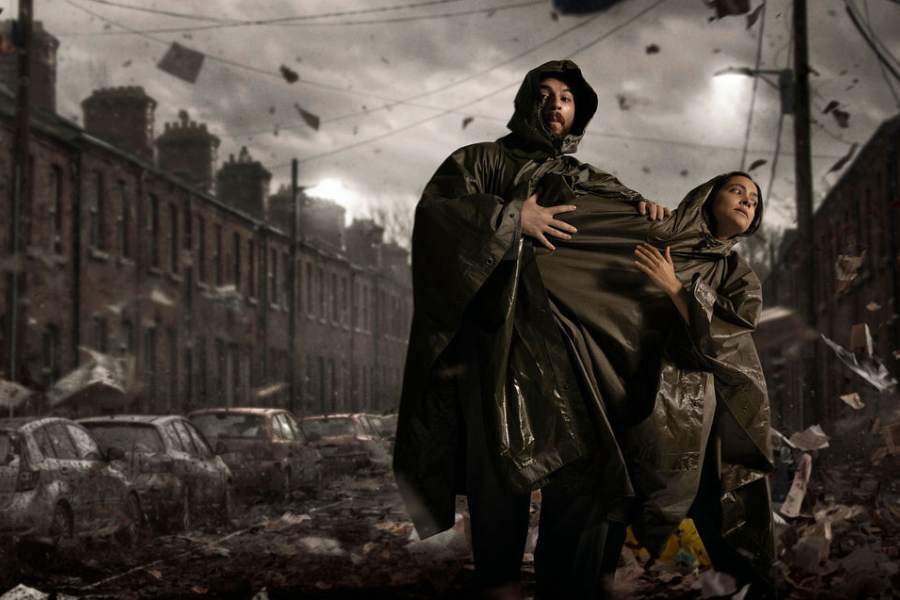 Two figures shrouded in capes stand in a stormy streetscape