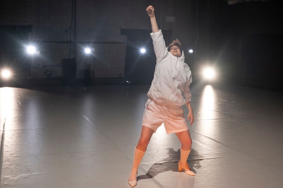 One dancer on a dark stage wearing white shorts lift her fist high above her head.