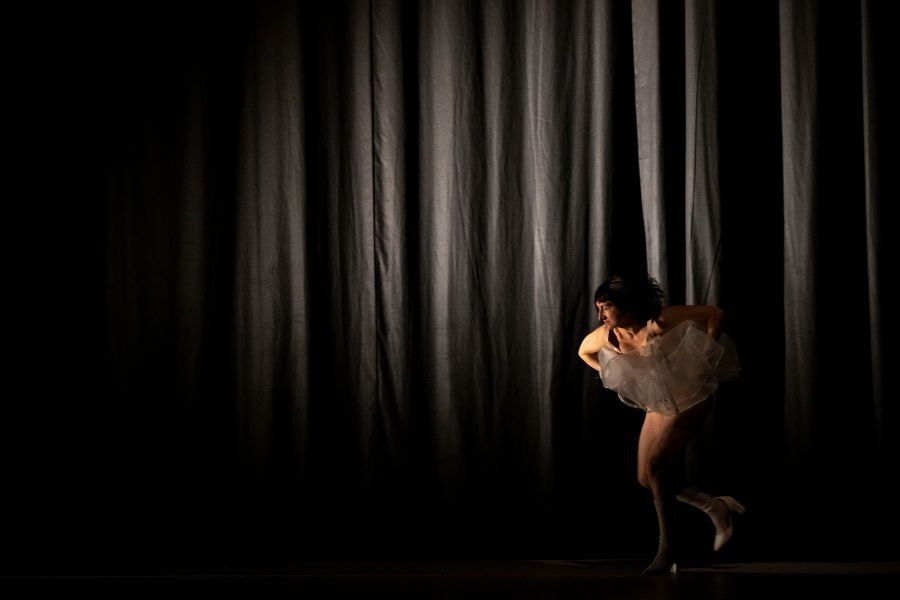 A figure in a white tutu on a dark stage