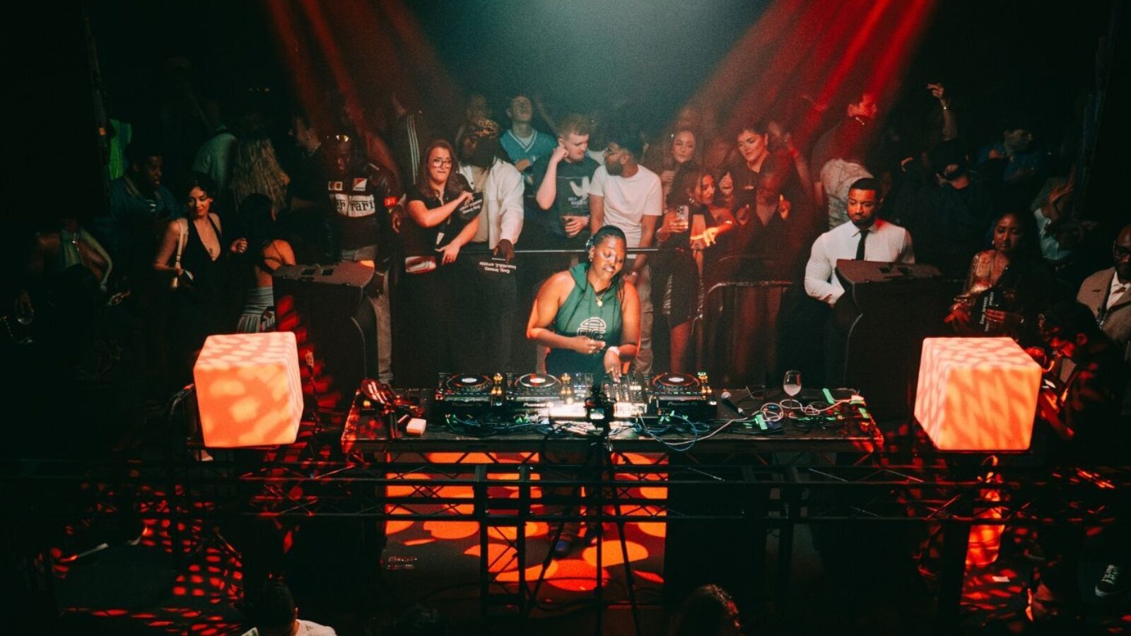 Club scene with DJ playing and the crowd dancing in the warm red glow of the lights