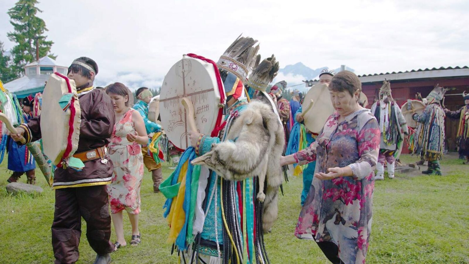 A group of people in shamanic outfits walk and play drums