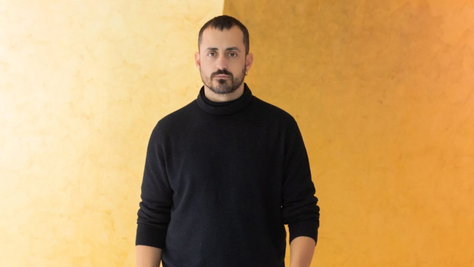 Portrait of Christos Papadopoulos standing in front of an orange and yellow background.
