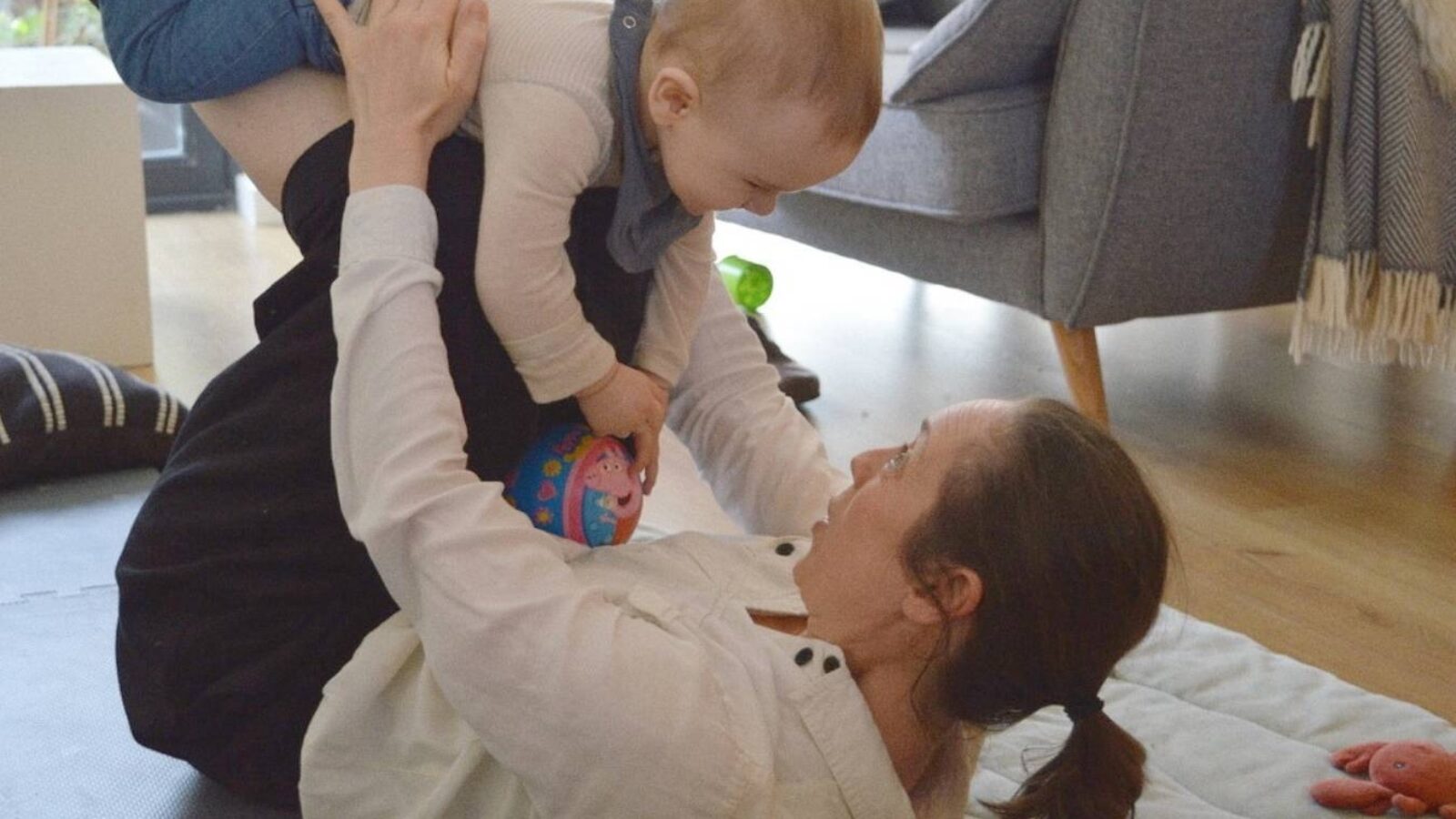 A mom lies on her back and lifts her baby in the air