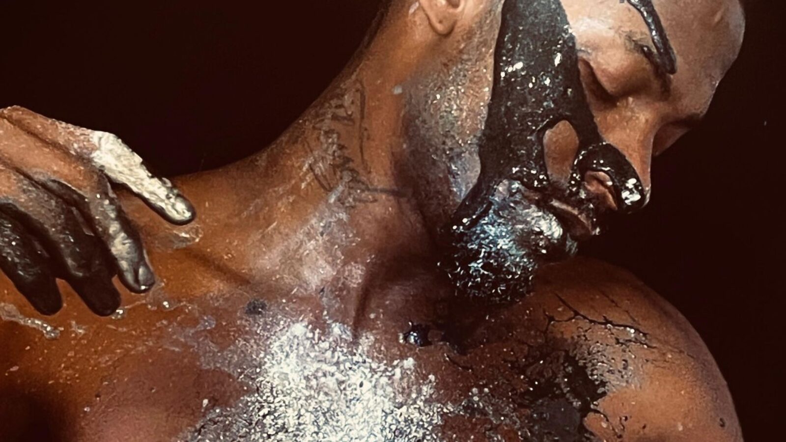 A man with dark skin streaked with shiny silver paint, shown from the showers up.