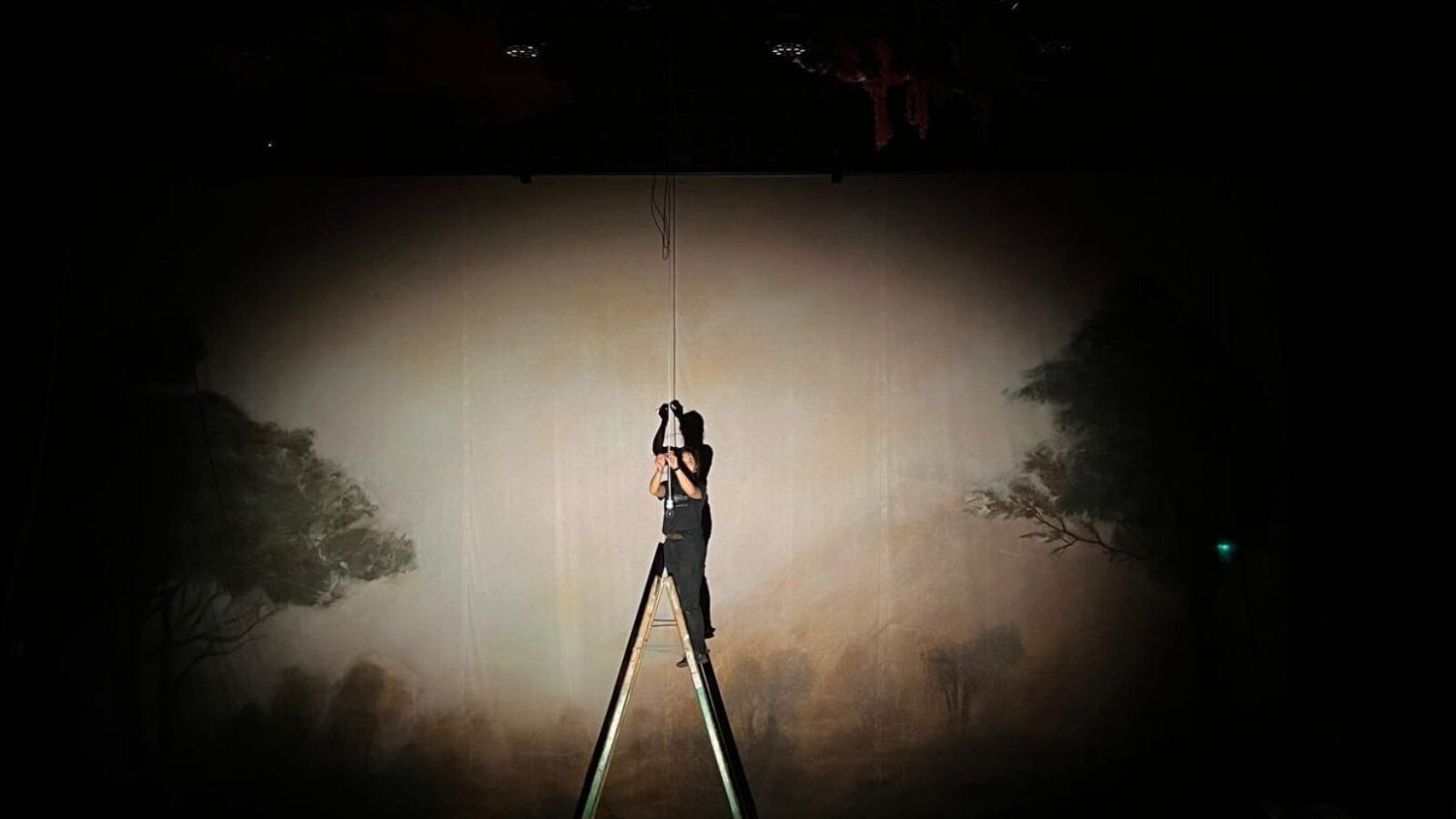 A dark stage with a spotlight on a person standing on a ladder.
