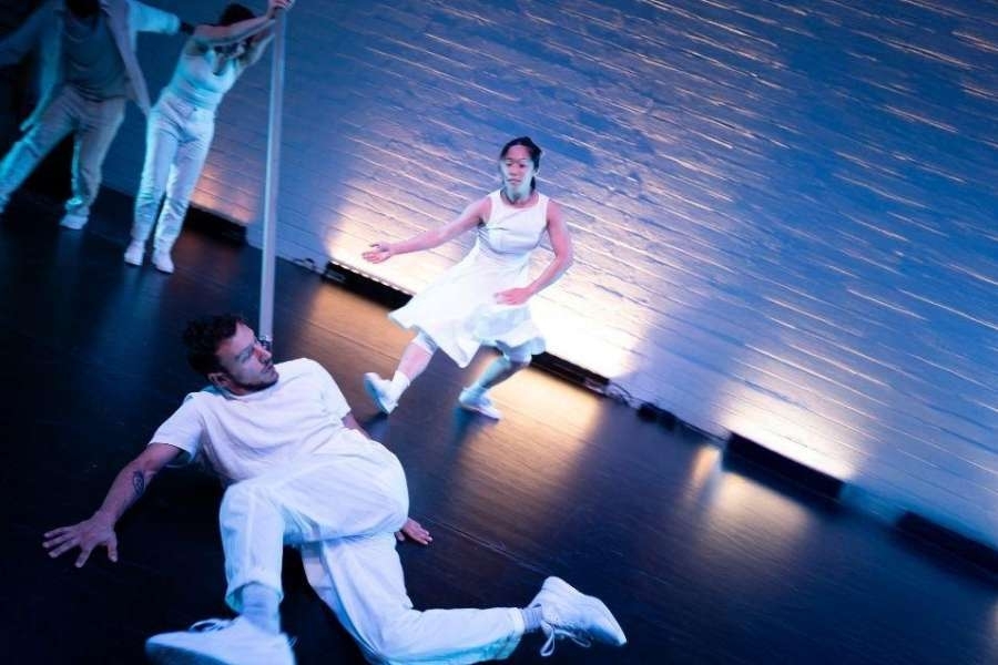 Dancers in white move, some standing and some on the floor