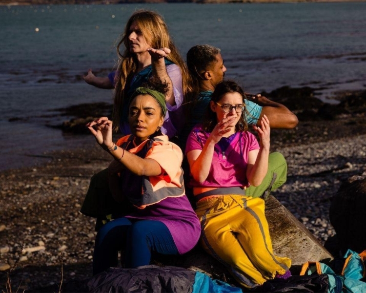 Four performers sit at the edge of the sea