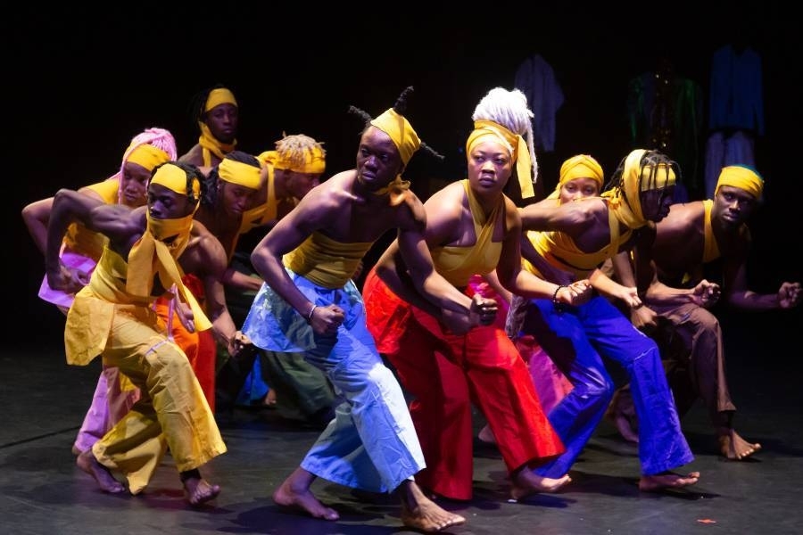 A group of performers create a tight formation wearing bright yellow and blue outfits with headdresses