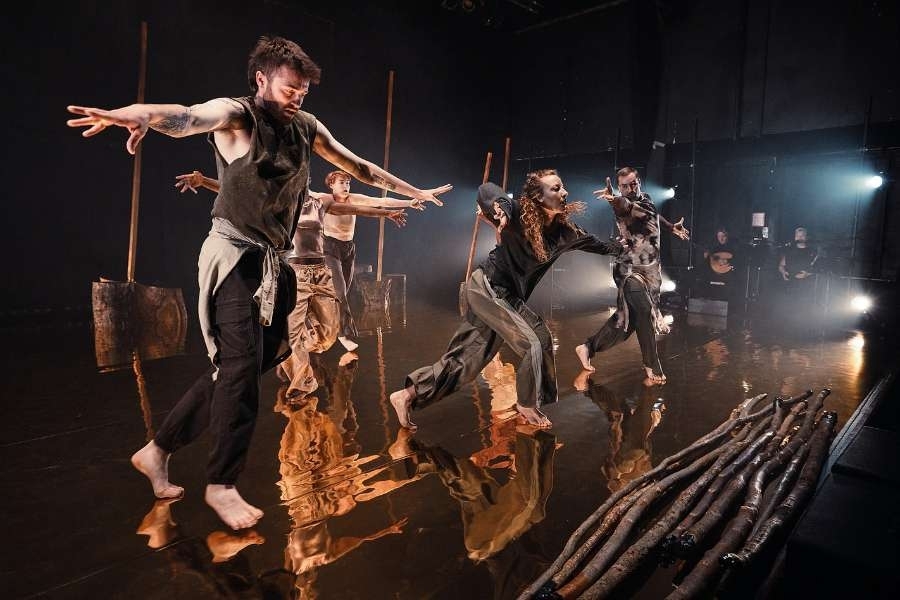 Two dancers carry a large piece of driftwood, one stooping forward, the other bending back