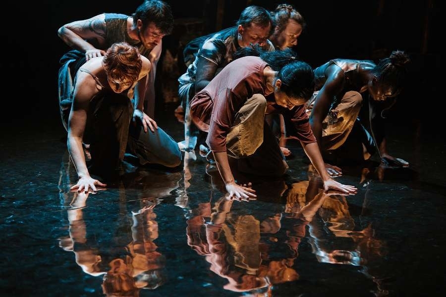 Group of people stand in a group in natural coloured clothing staring with intense expressions