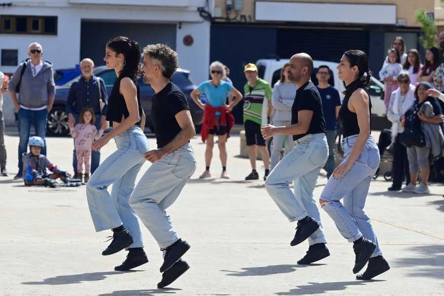 Four people in jeans and black tops perform in unison outdoors
