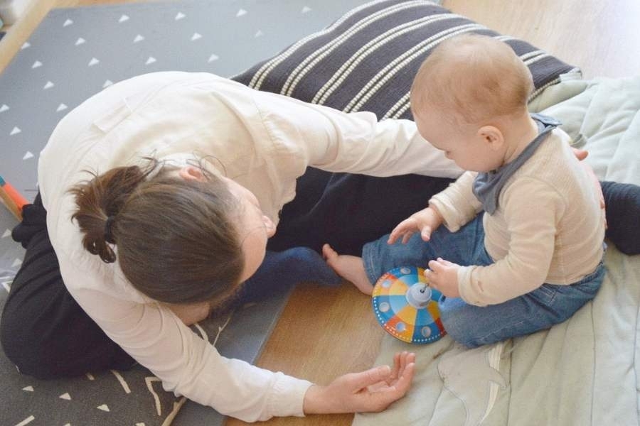 A woman and baby sit together on the floor together playing