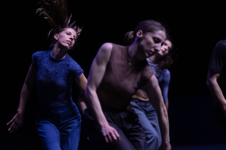 Group of dancers move and leap with great energy against a dark background.