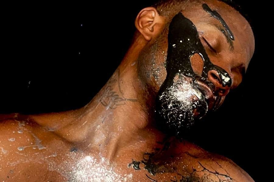 A man with dark skin streaked with shiny silver paint, shown from the showers up.