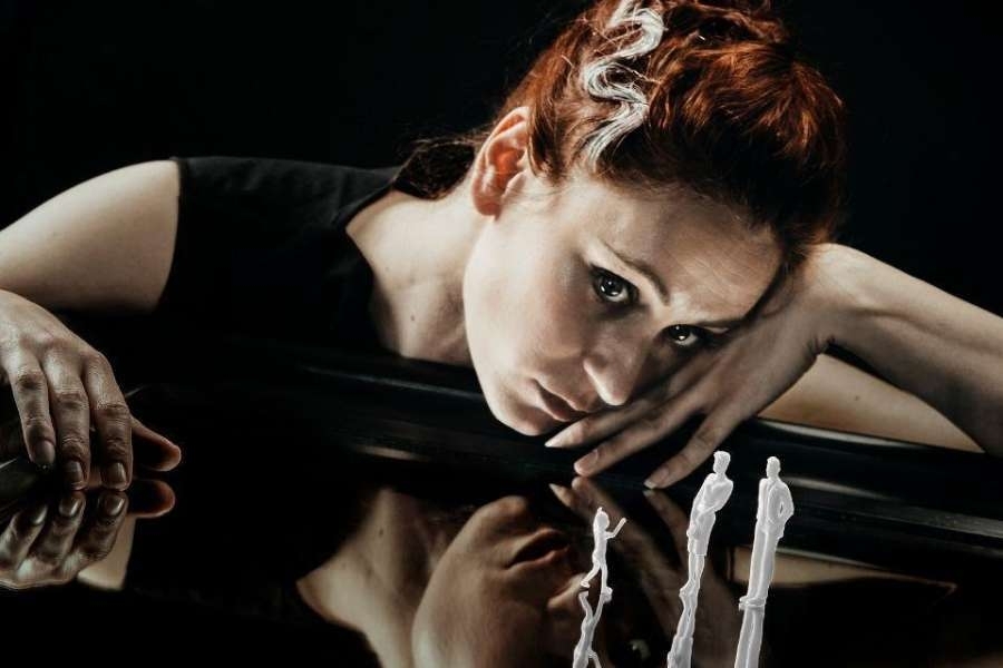 Close-up of a woman resting her arms and head on a reflective table with small toy people in the foreground