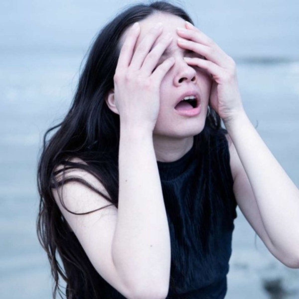 A woman, open-mouthed, covers her eyes with her hands