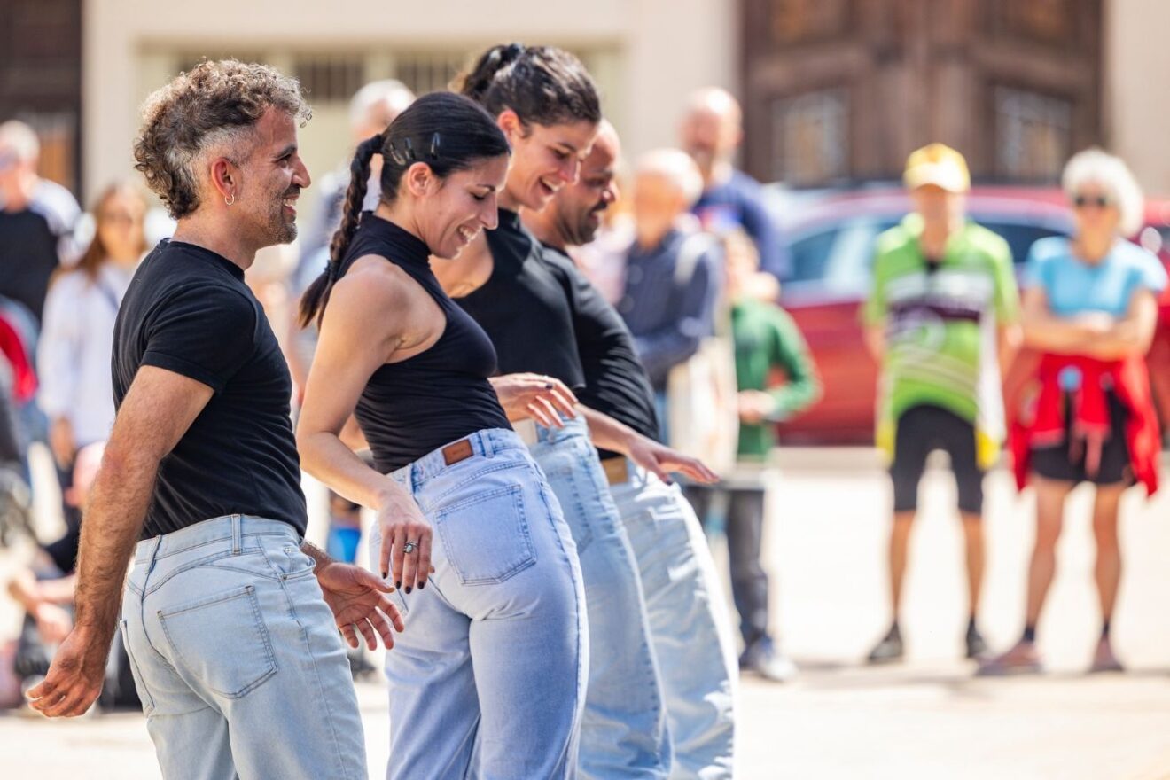Four people in jeans and black tops perform in unison outdoors
