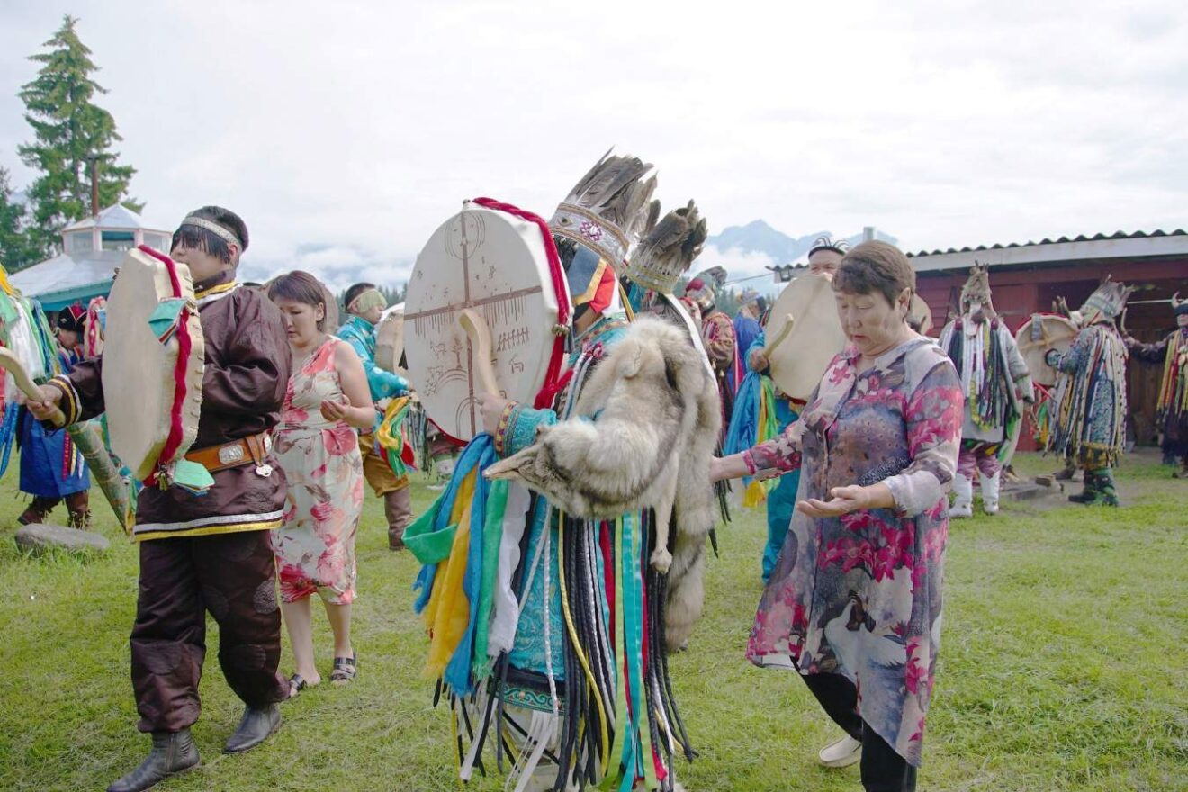 A group of people in shamanic outfits walk and play drums