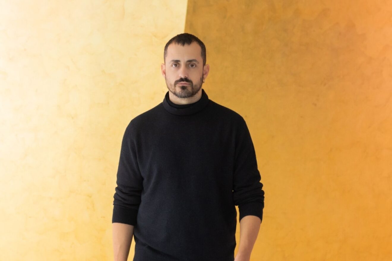 Portrait of Christos Papadopoulos standing in front of an orange and yellow background.