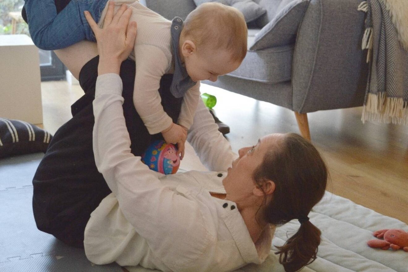 A mom lies on her back and lifts her baby in the air