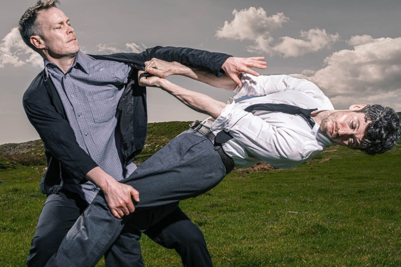 Two people pull at each other leaning back and counterbalancing, outdoors in a field