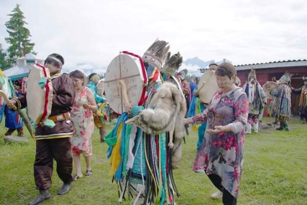 A group of people in shamanic outfits walk and play drums