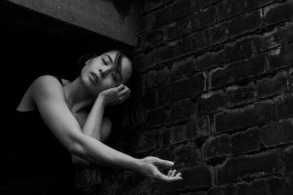 A woman stretches her arms out front, resting one on top of the other and has her eyes closed.